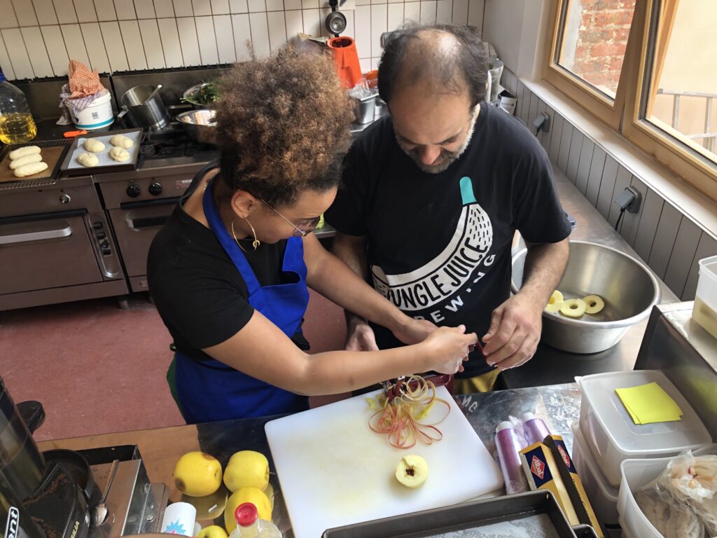 Photos couleur illustrant le travail bénévole collaboratif autour de la cuisine à la Coco Cantine, restaurant associatif du 20ème arrondissement de Paris qui s'attèle aux problématiques de l'accessibilité du bien manger et de l'alimentation durable pour toustes. - Initiation au pèle-pommes.