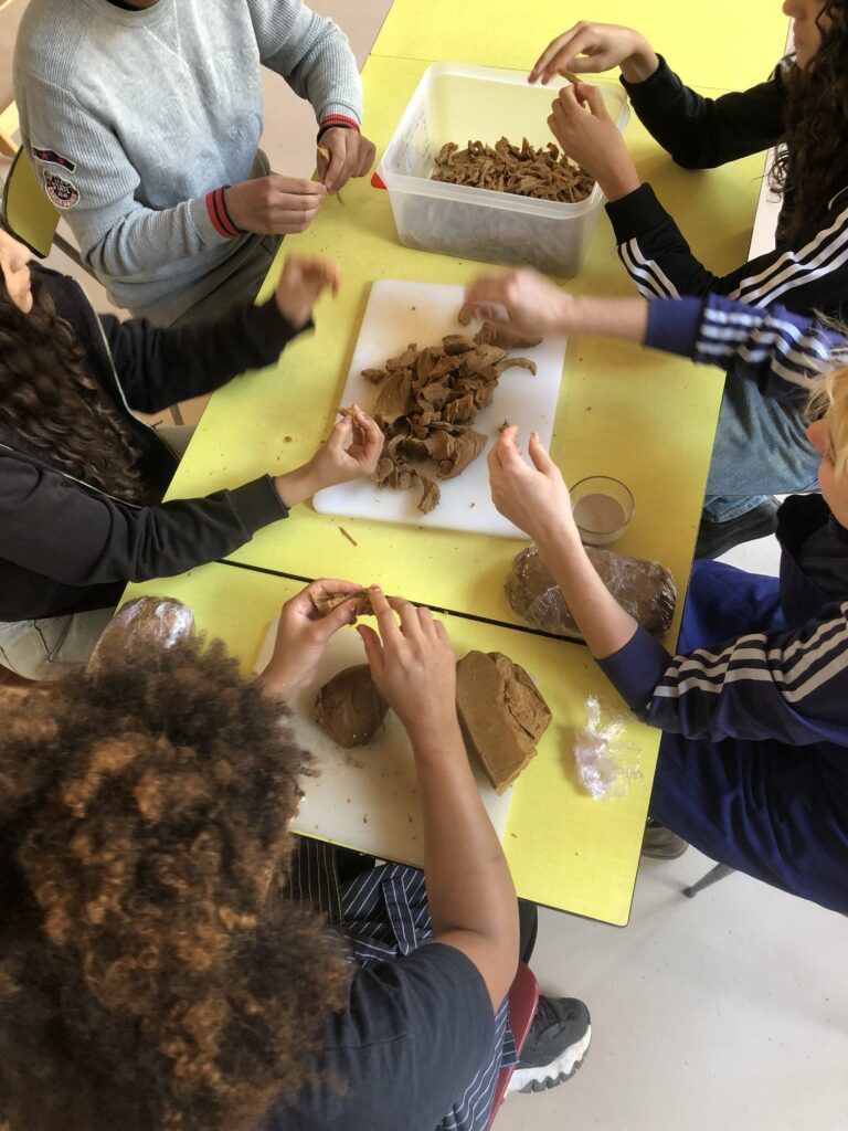 Photos couleur illustrant le travail bénévole collaboratif autour de la cuisine à la Coco Cantine, restaurant associatif du 20ème arrondissement de Paris qui s'attèle aux problématiques de l'accessibilité du bien manger et de l'alimentation durable pour toustes. - Mise en miette collective du seitan, autour d'une table, par l'équipe de salarié•es et bénévoles