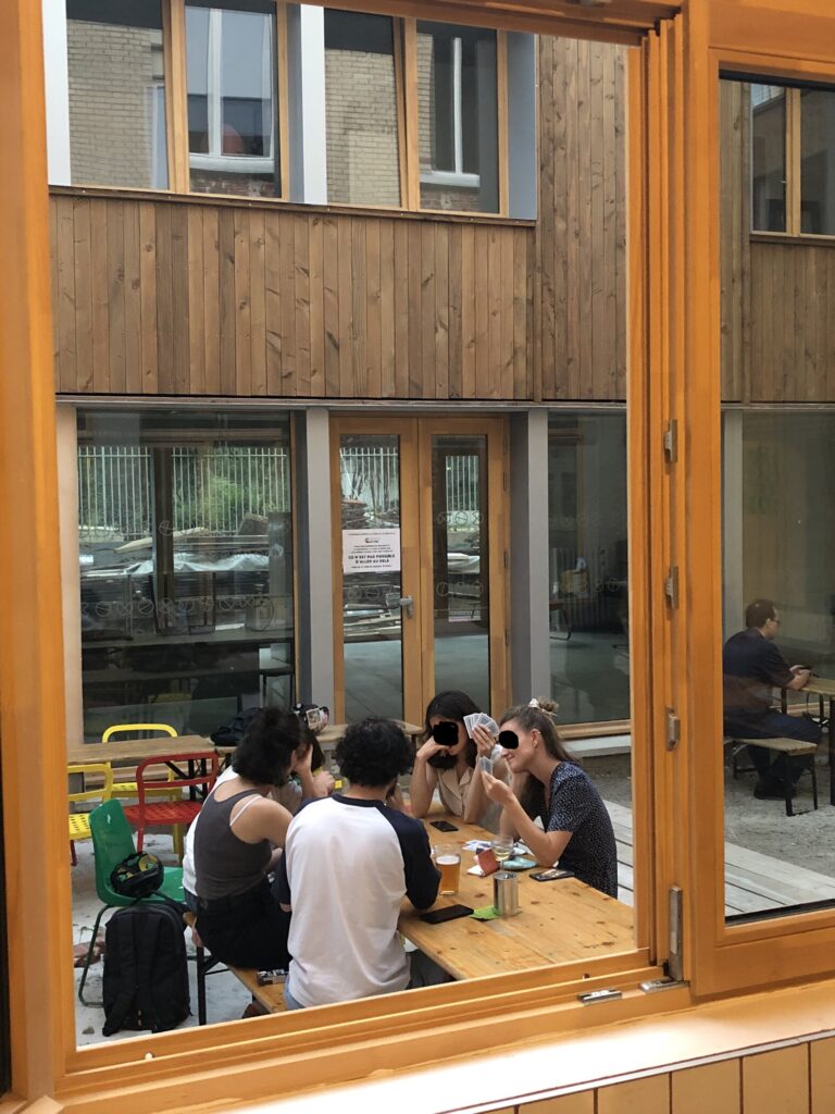 Photo d'un groupe d'adultes jouant aux cartes sur la terrasse de la Coco cantine, restaurant associatif végétarien pour toustes à Place des fêtes, entre le 19ème et le 20ème arrondissement de Paris