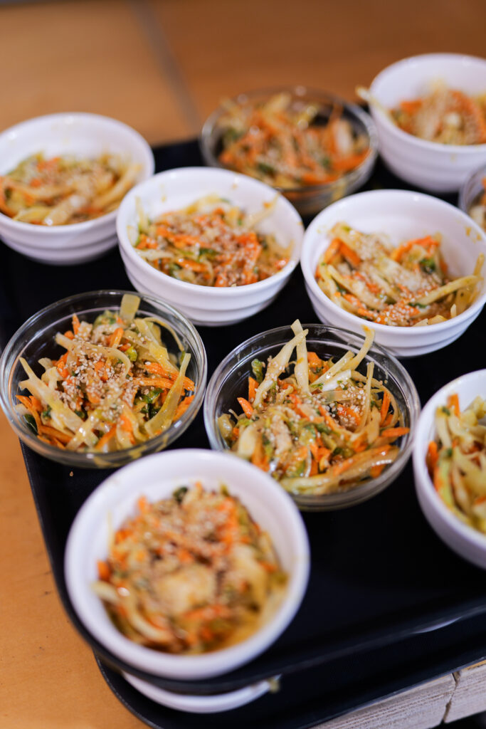 Photo de plat végétarien/végan de la Coco caantine, restaurant engagé dans le 20ème arrondissement de Paris. Elle est prise par Claire Migeon. On y voit un plateau noir sur lequel sont disposés des récipients remplis d'une salade composée simple et colorée qui correspond au "bien manger" accessible revendiqué par l'association.